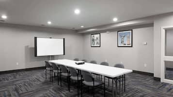 Un salón de conferencias con una larga mesa, seis sillas, una pantalla de proyector y dos cuadros en la pared.