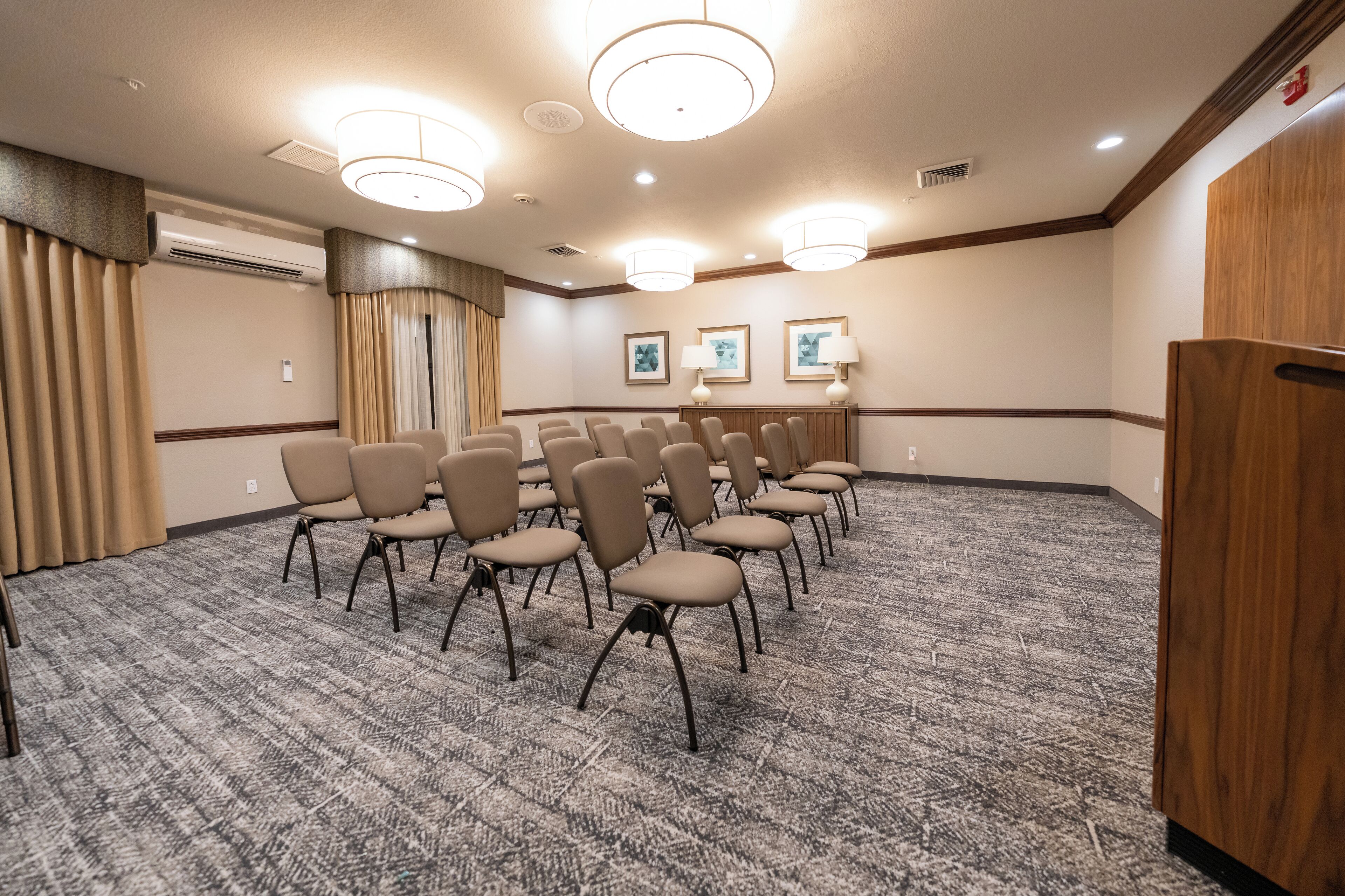 A conference room with rows of chairs, a carpeted floor, and wall-mounted lamps.