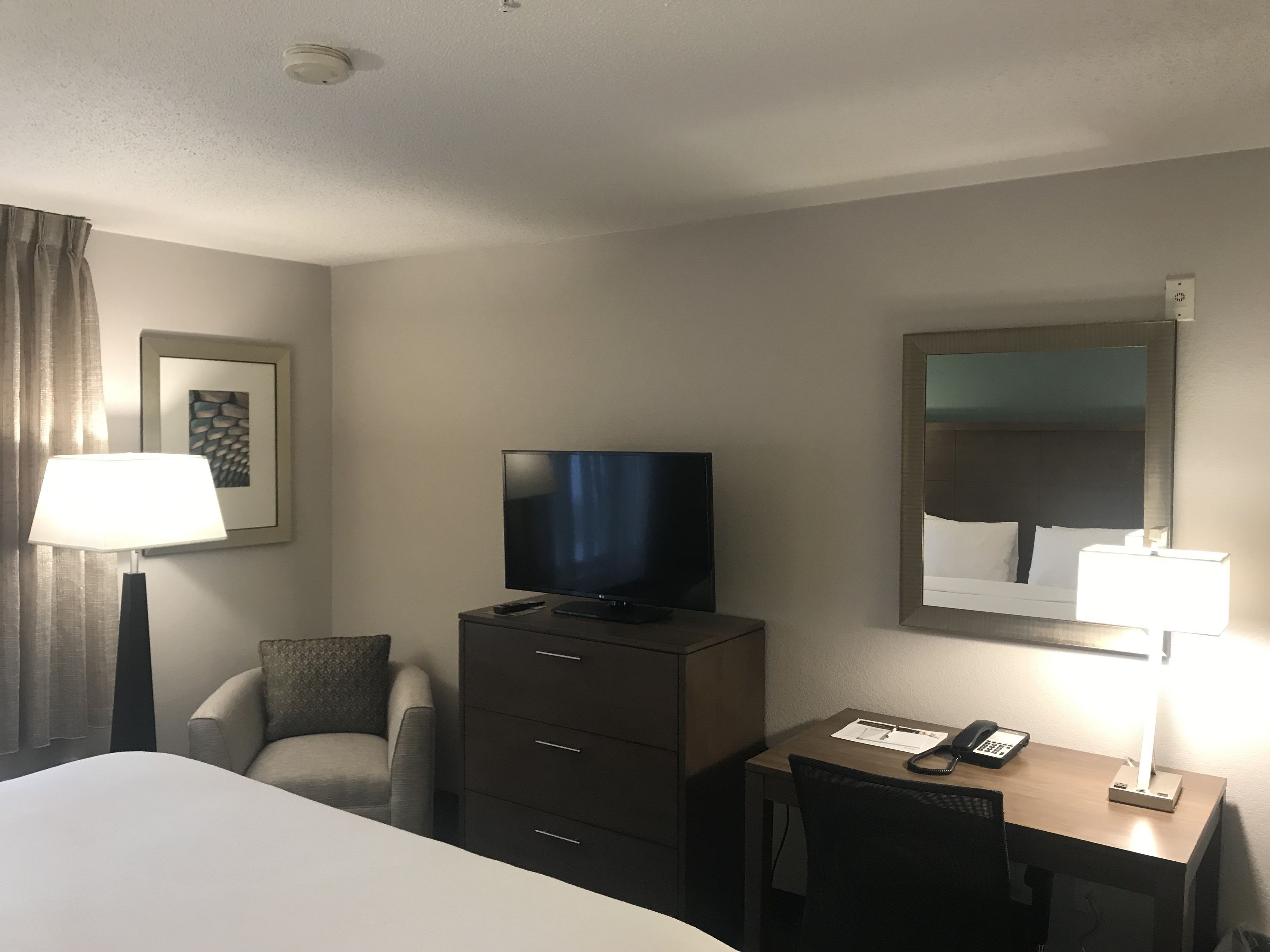A hotel room with a bed, a desk with a telephone, a television, a chair, a lamp, and a framed picture on the wall.