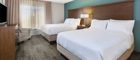 A hotel room with two beds, a desk with a TV, a chair, and a large window with curtains.