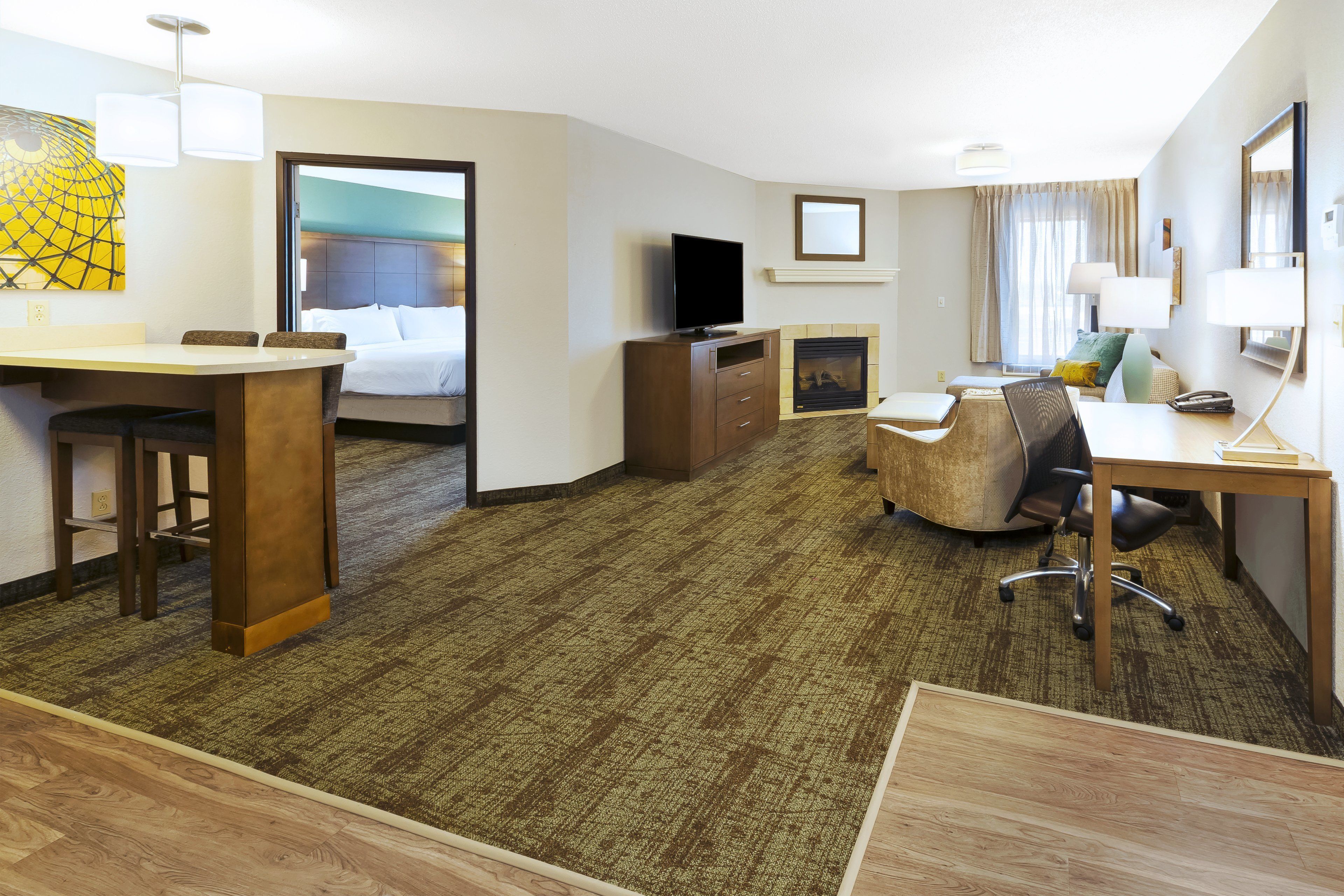 A hotel room with a bed, desk, TV, and a fireplace.