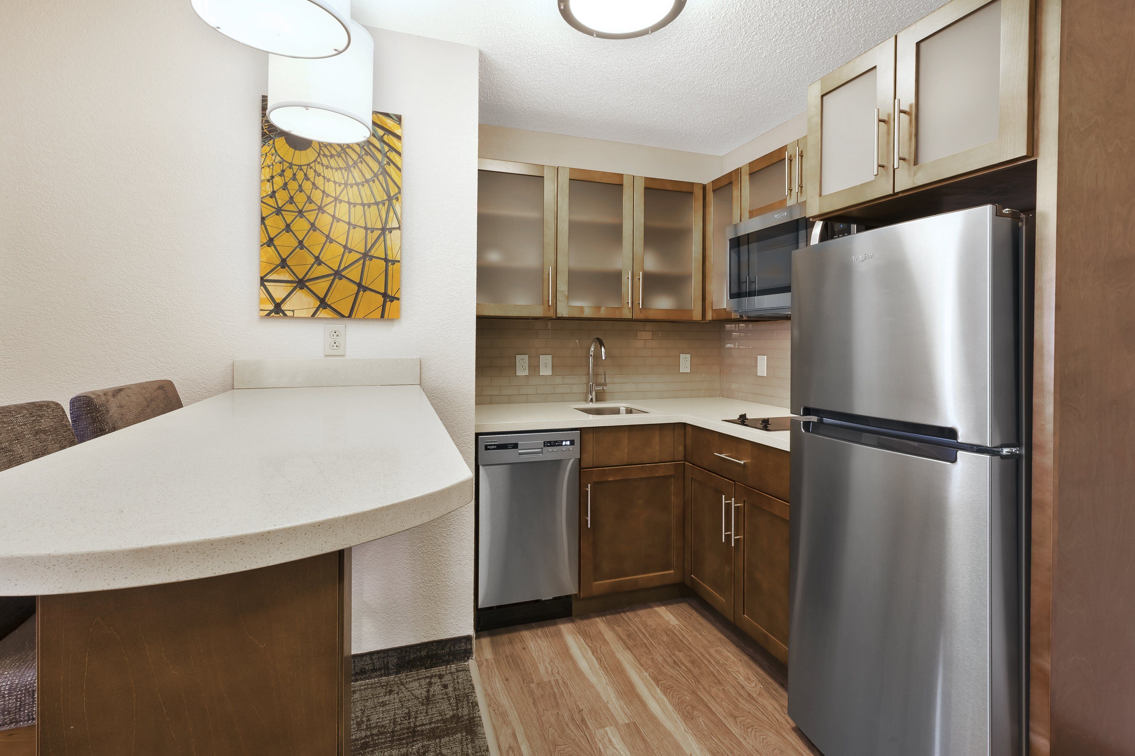 A modern kitchen with wooden cabinets, stainless steel appliances, and a white countertop.