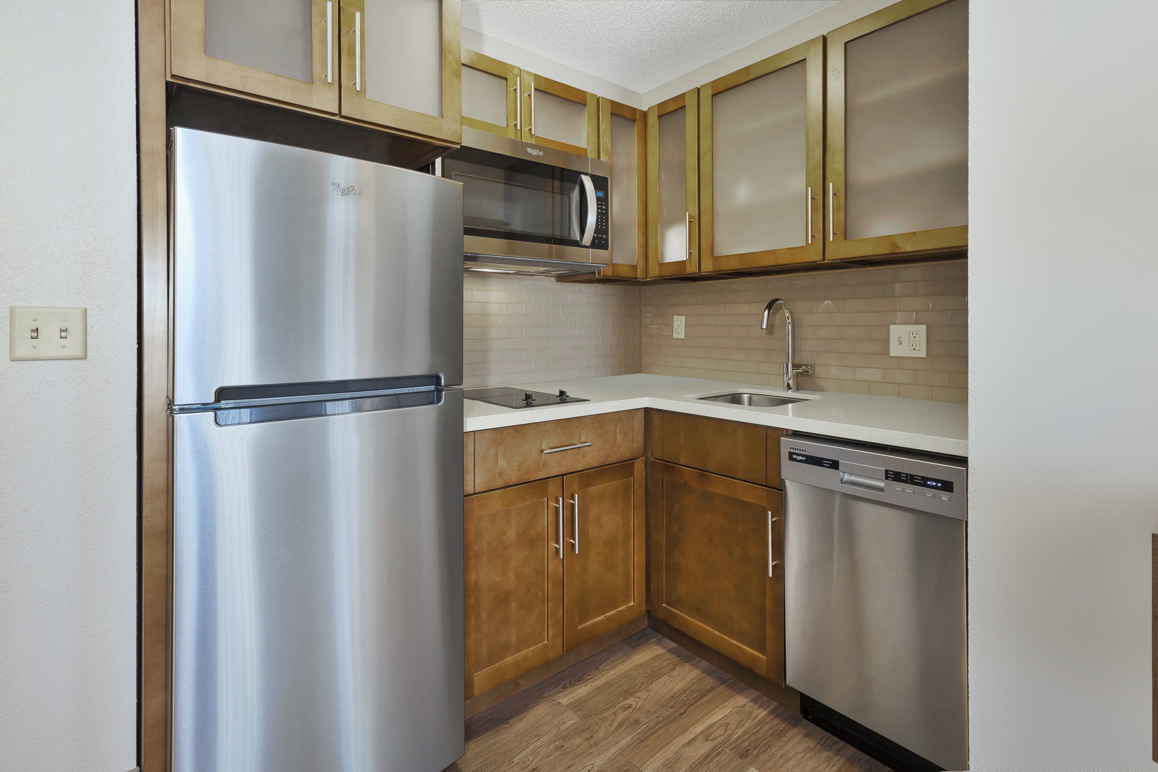 A kitchen with stainless steel appliances, wooden cabinets, and a tiled backsplash.
