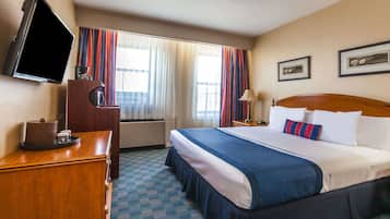 A hotel room with a bed, a TV, a desk, a lamp, and a window with curtains.