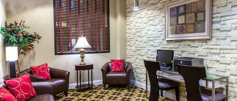 A room with a patterned carpet, leather sofas, a desk with a computer, and a wall-mounted TV.