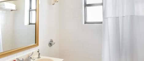 Une salle de bain équipée d’un lavabo, d’un miroir, d’une douche et d’une fenêtre.