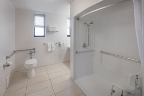 A bathroom with a toilet, a shower with a grab bar, a window, and a towel rack. - Ramada by Wyndham Jersey City (Jersey City)