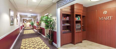 A hotel corridor with a patterned carpet, wooden walls, and a visible 'MART' sign indicating a store or restaurant.