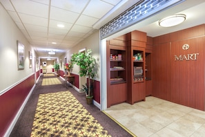 Un pasillo de hotel con alfombra estampada, paredes de madera y un letrero visible que dice 'MART', indicando una tienda.