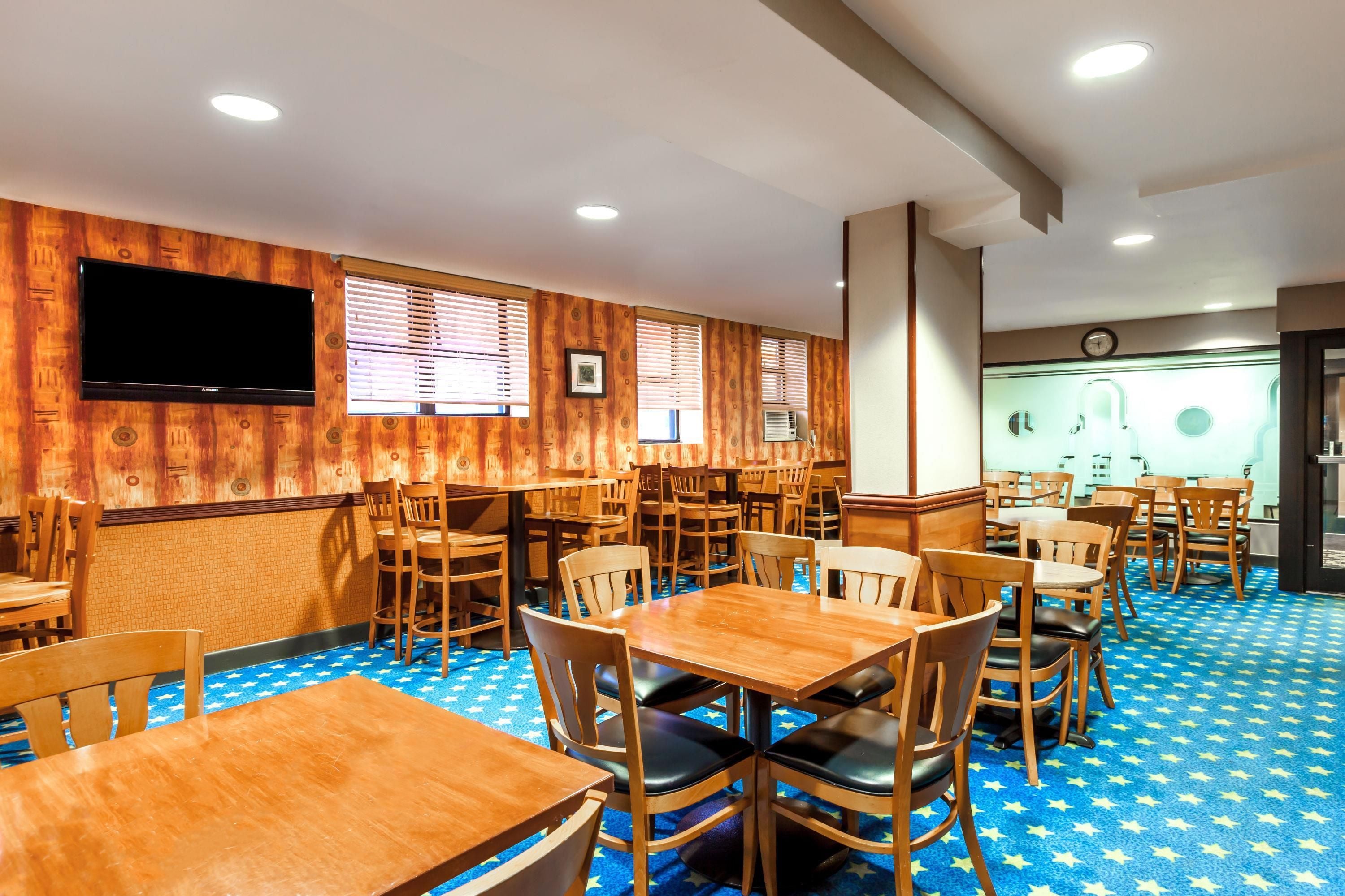 Un restaurant aux murs recouverts de lambris en bois, avec de nombreuses tables et chaises, un téléviseur à écran plat fixé au mur et une horloge au mur.
