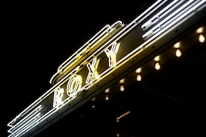 A neon sign with the letters "ROXY" in a stylized font, mounted on a metal structure.