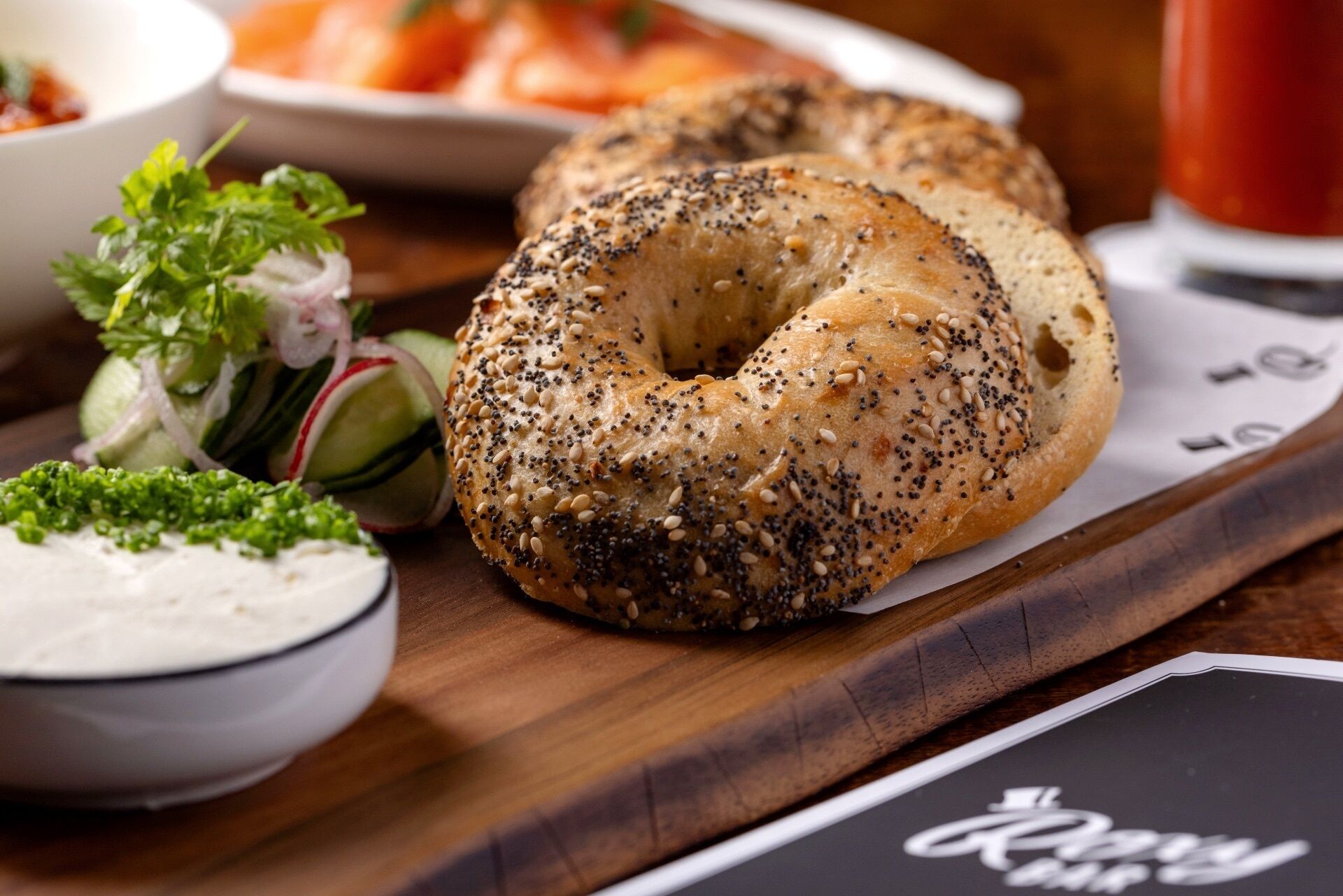 A bagel with sesame and poppy seeds, accompanied by a small salad and a cup of tea.