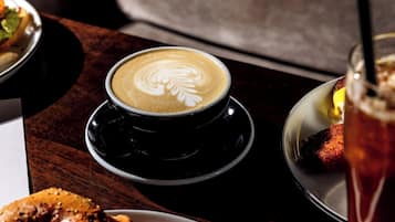 A cup of coffee with latte art on a saucer, a plate with a food item, and a glass of a beverage with a garnish.