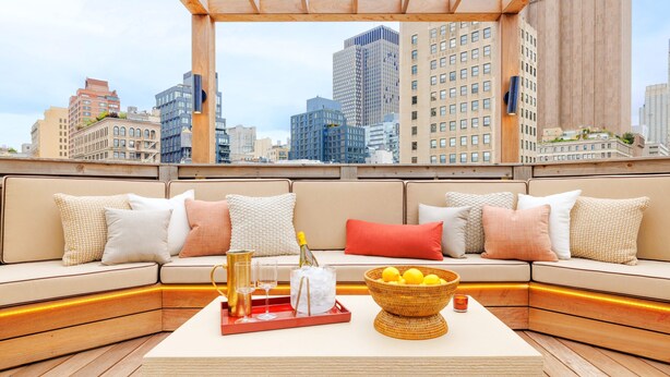 A rooftop lounge with a city view, a sofa set, a tray with glasses and a bottle, and a basket of lemons. - Roxy Hotel New York (New York)