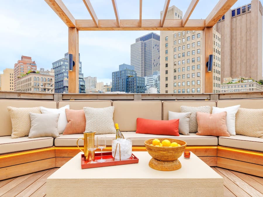 A rooftop lounge with a city view, a sofa set, a tray with glasses and a bottle, and a basket of lemons.