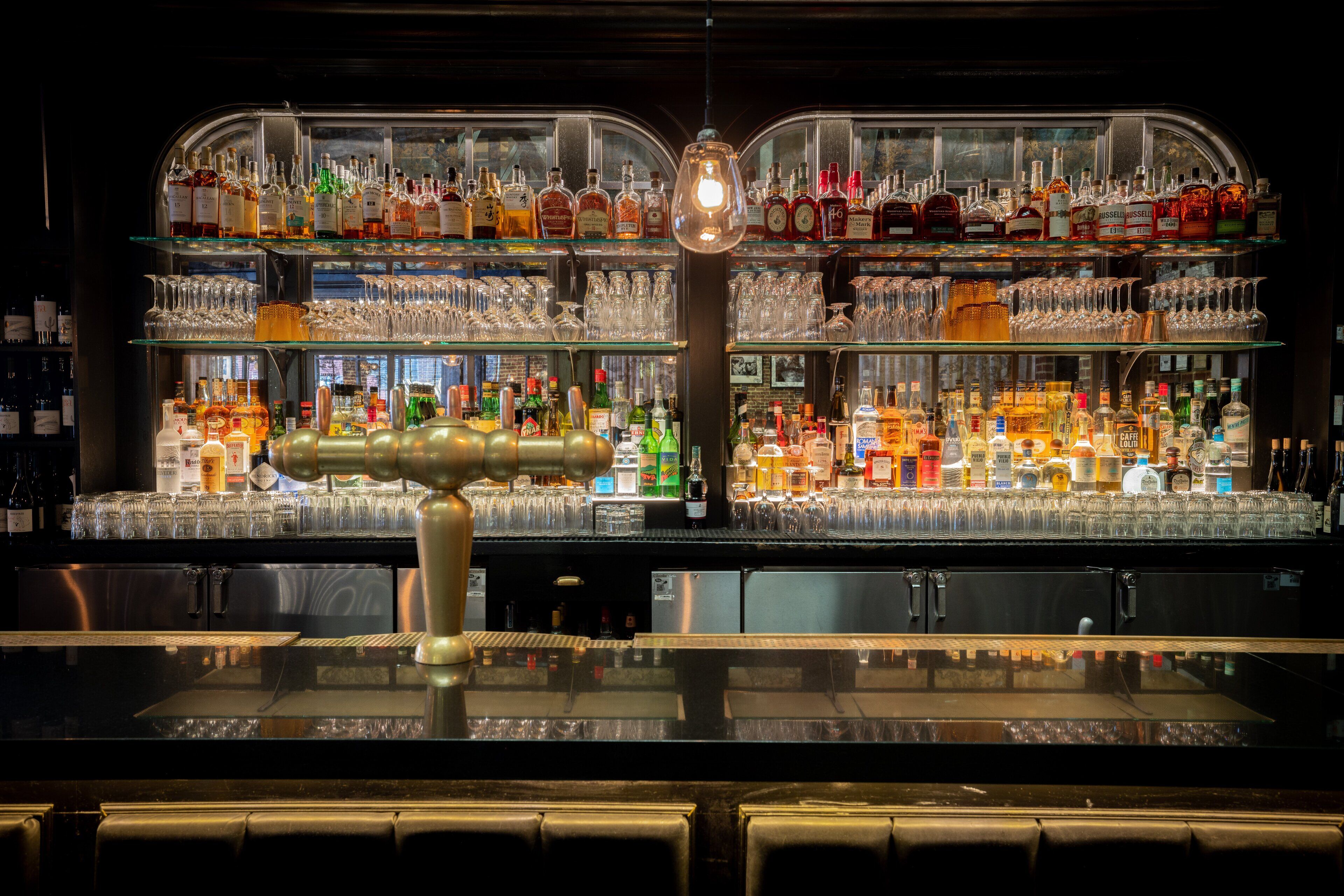 Un espace bar avec des étagères remplies de bouteilles d’alcool et de verres.