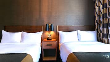 Una habitación de hotel con dos camas, una mesita de noche con lámpara y un papel tapiz estampado.