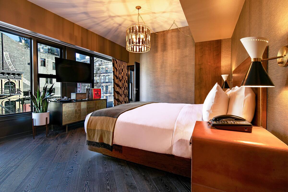 A modern hotel room with a large bed, a desk, a TV, and a view of the city.