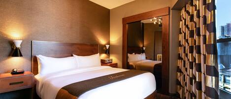 A hotel room with a large bed, a nightstand with a lamp, a mirror, and a view of the city through the window.