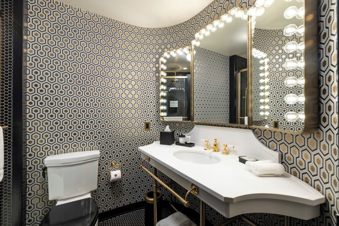 A bathroom with a white sink, gold faucets, and a mirror with lights.