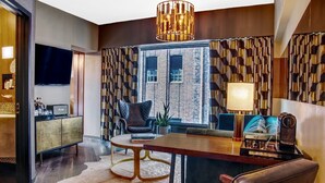 A modern living room with a large wooden dining table, a comfortable sofa, a black leather armchair, and a television on a wooden cabinet. - Roxy Hotel New York (New York)