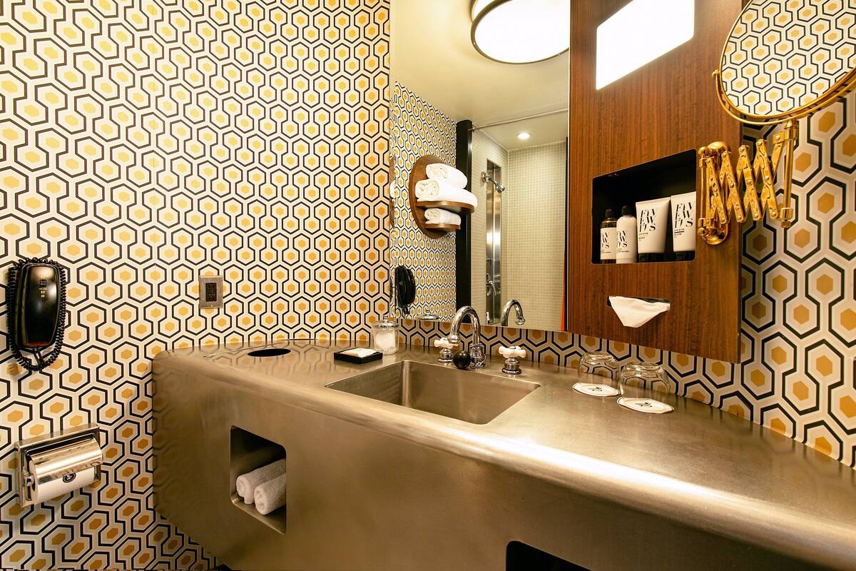 A modern bathroom with a geometric patterned wall, a stainless steel sink, and a mirror with a towel rack.