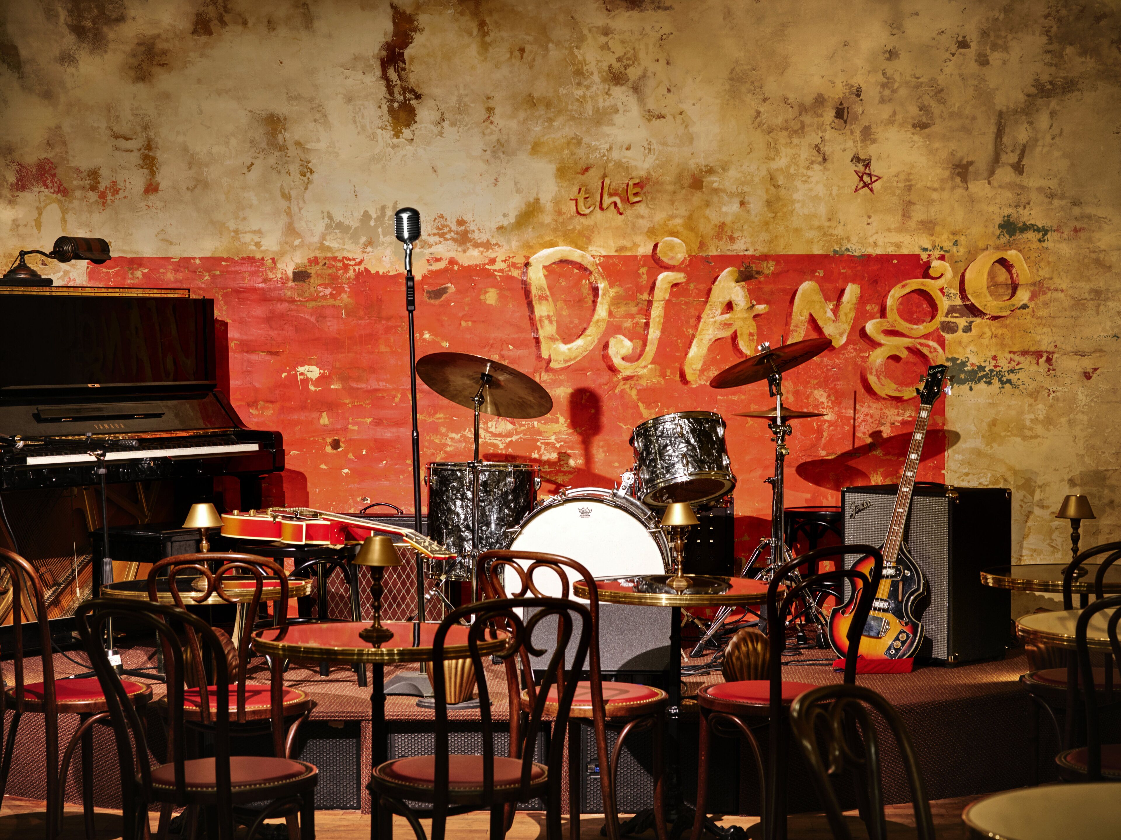 A jazz club interior with a piano, drum set, and tables with chairs.