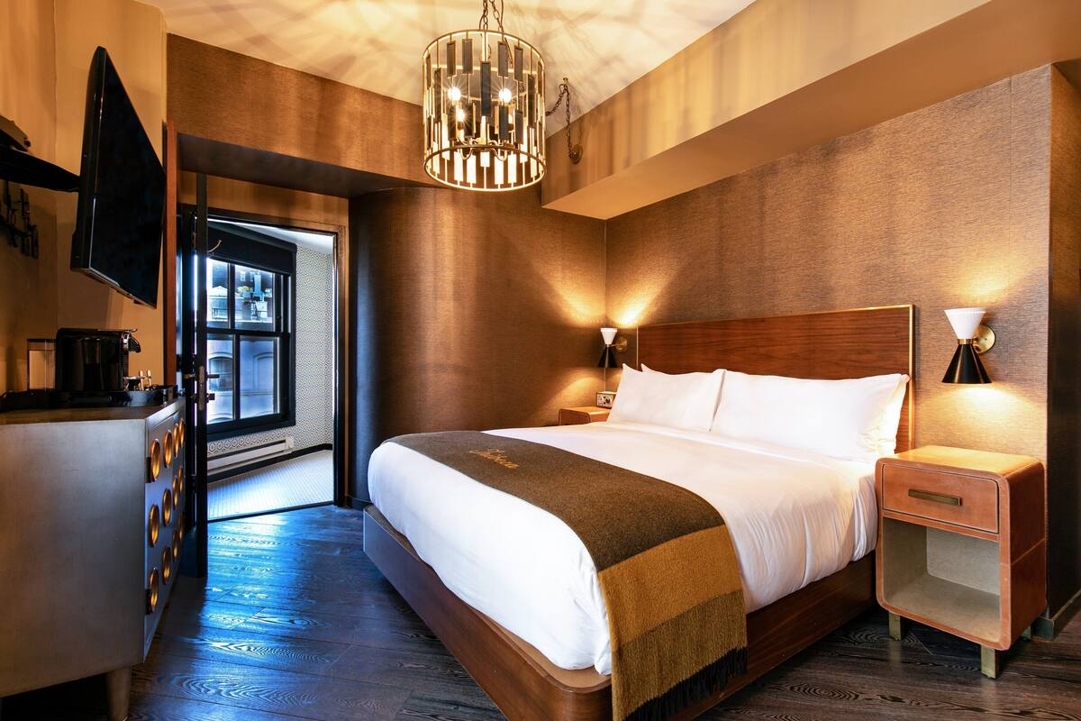 A modern hotel room with a large bed, bedside lamps, a TV, and a view of the outside.