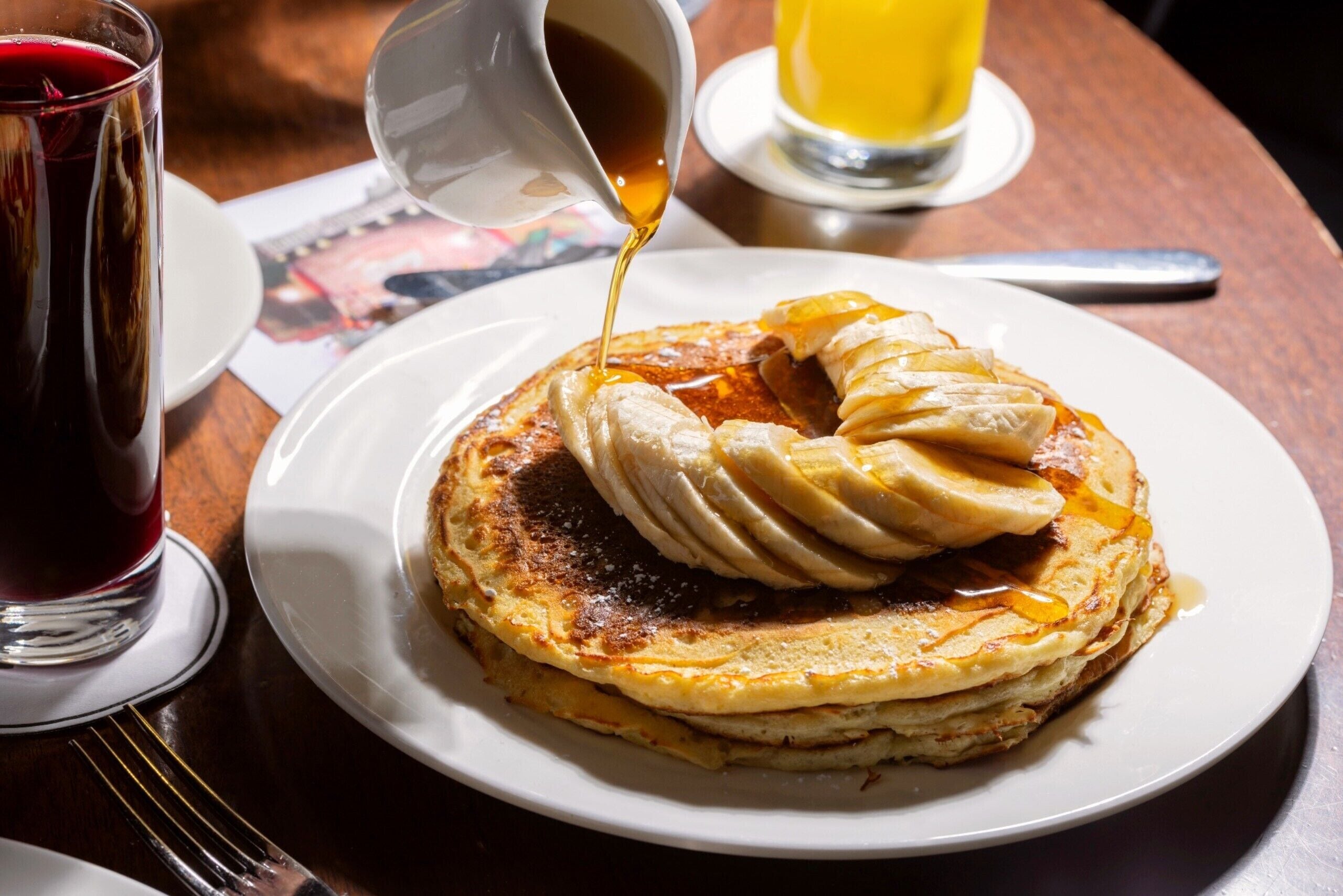 Una pila di pancake con sciroppo che viene versato sopra, servita su un piatto bianco.
