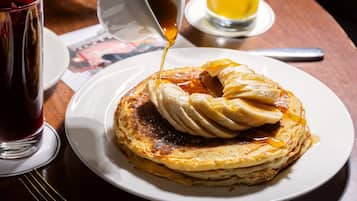 Una pila di pancake con sciroppo che viene versato sopra, servita su un piatto bianco.