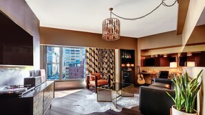 A modern living room with a large window, a glass coffee table, a sofa, a chair, and a potted plant. - Roxy Hotel New York (New York)
