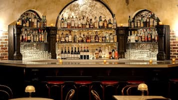 A bar with a brick wall backdrop, shelves stocked with various liquor bottles, and several stools and tables.