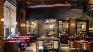 A spacious restaurant with brick walls, leather seating, and a bar area. - Roxy Hotel New York (New York)
