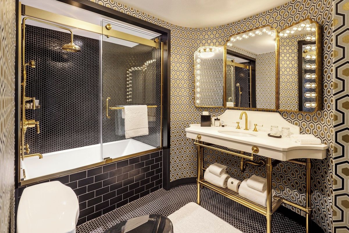 A bathroom with a black and white patterned wall, a gold-framed vanity, and a glass-enclosed shower area.