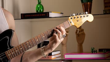 A person playing an electric guitar in a room with bookshelves, a green sculpture, and a wooden bust on display.