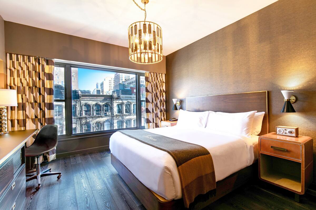 A modern hotel room with a large bed, a desk, and a view of the city.