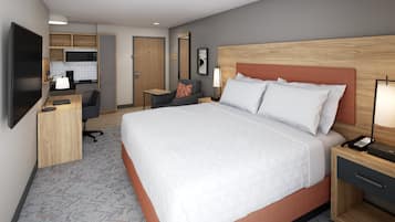 A hotel room with a large bed, a desk with a chair, a TV, a small kitchenette, and a bathroom door.