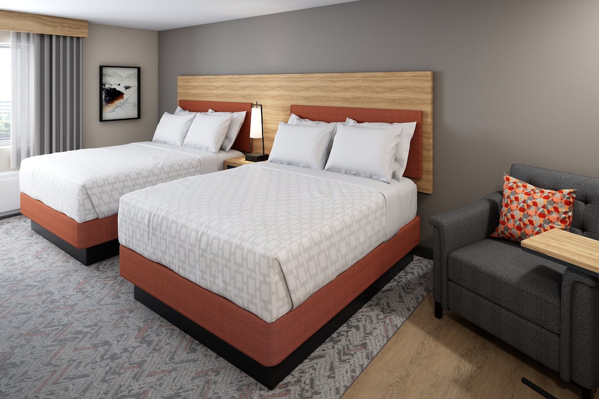 Habitación de hotel con dos camas, un sofá, una mesita de noche y una lámpara fijada a la pared.