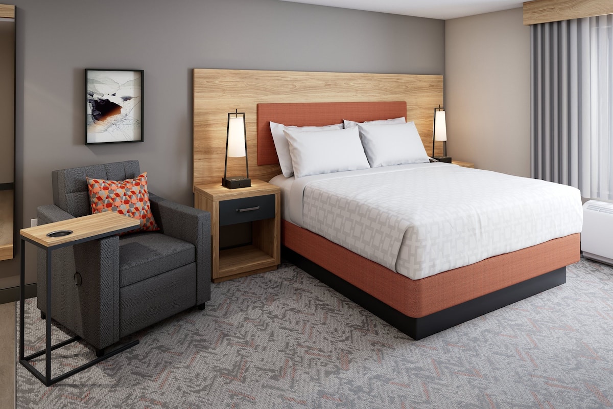 Una habitación de hotel moderna con una cama grande, un sofá, una mesita de noche y una lámpara de pared.