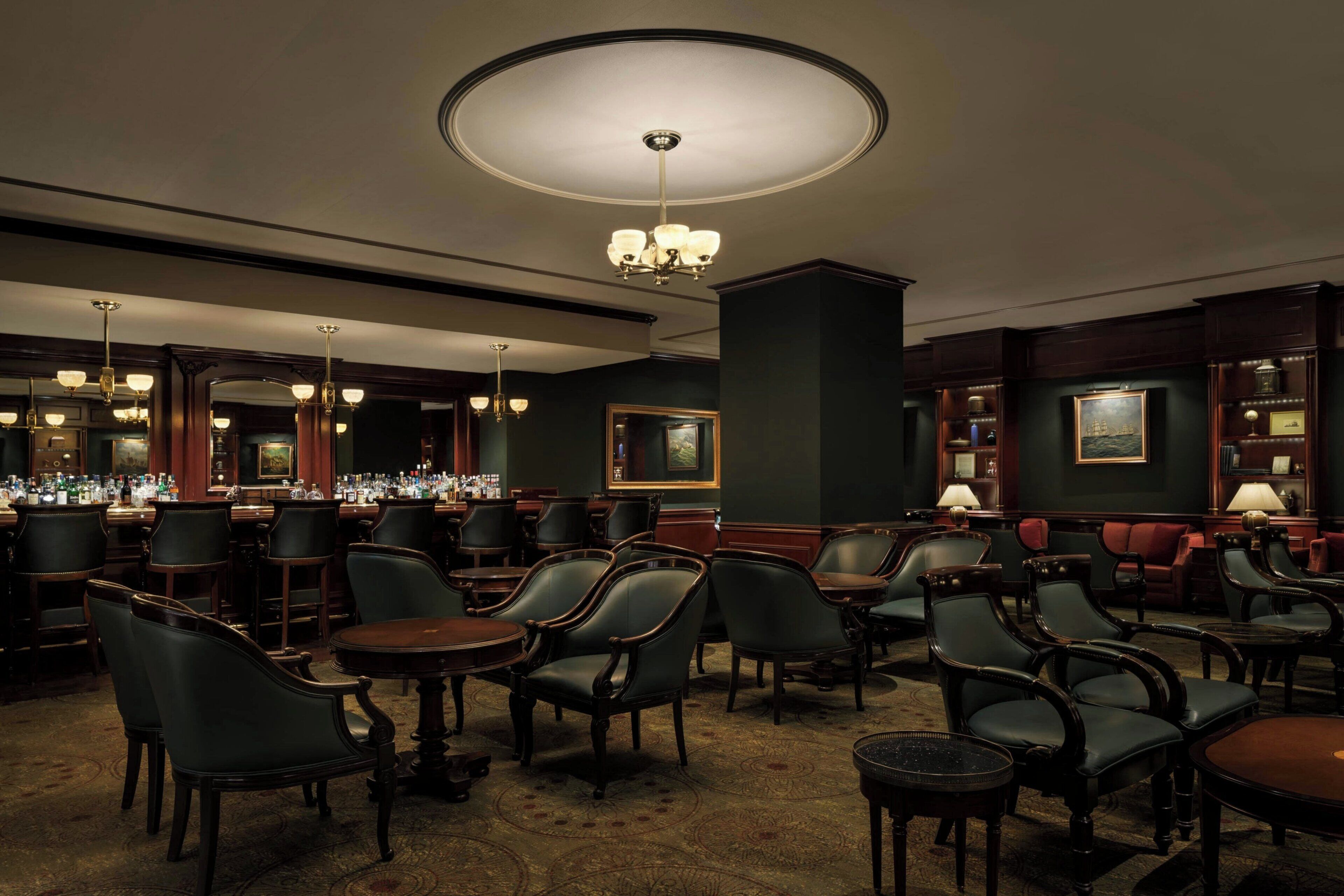 A bar area with multiple seating arrangements, including round tables and chairs, and a chandelier.