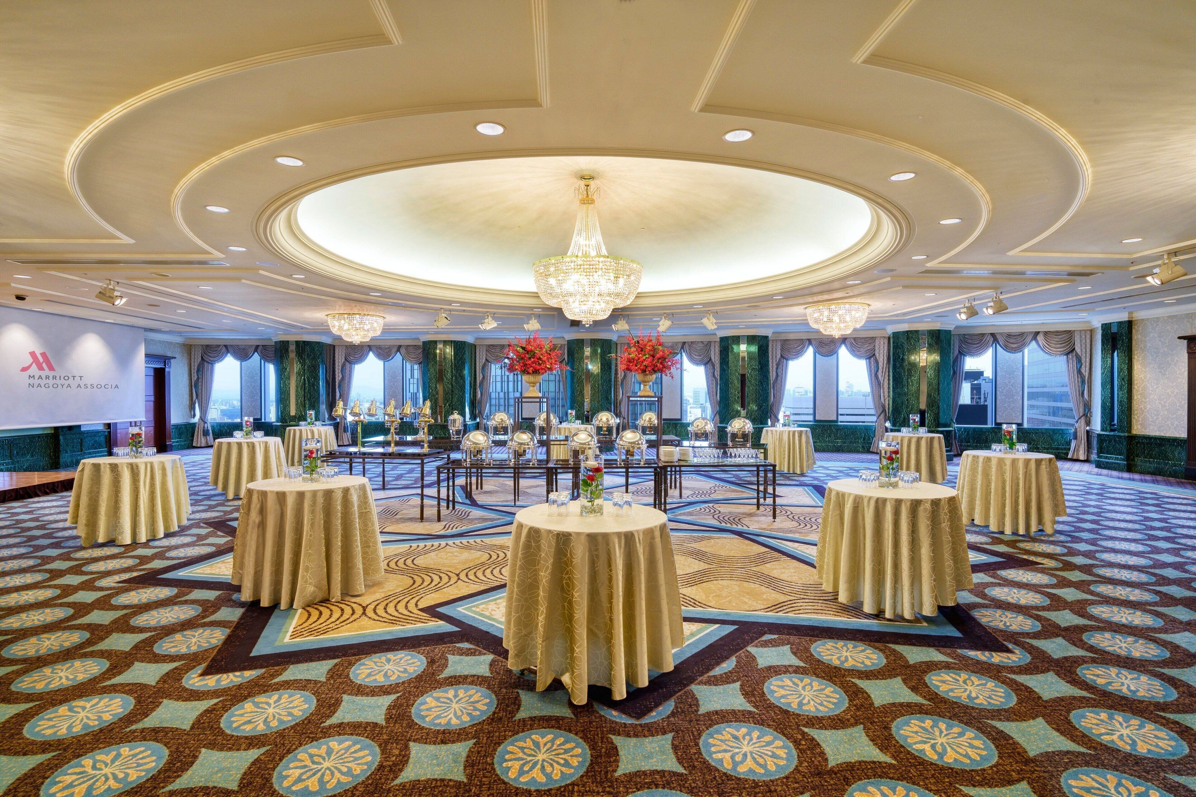 A spacious banquet hall with round tables, a large chandelier, and a patterned carpet.
