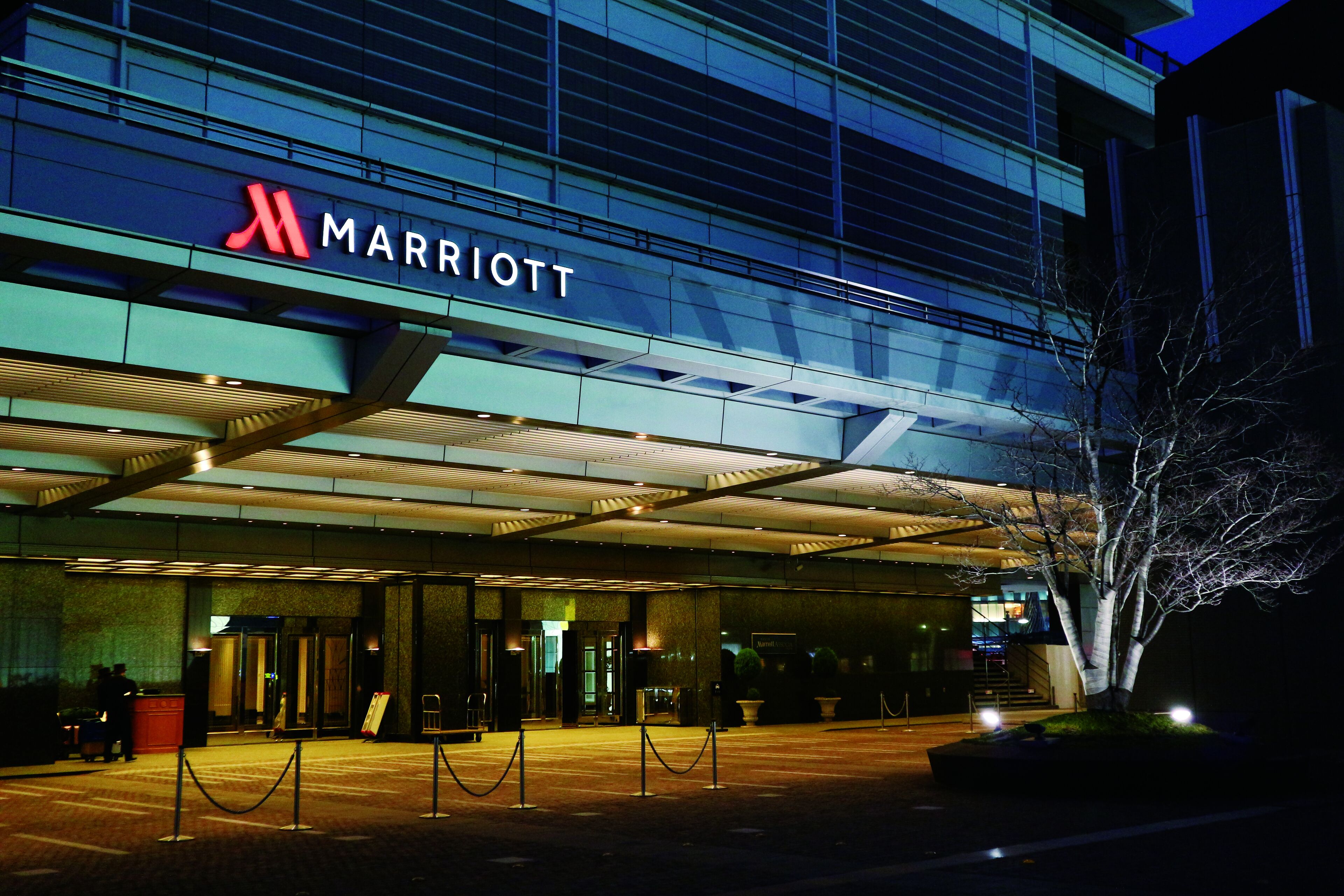 A Marriott hotel entrance with a modern glass facade, a visible entrance, and a security barrier.