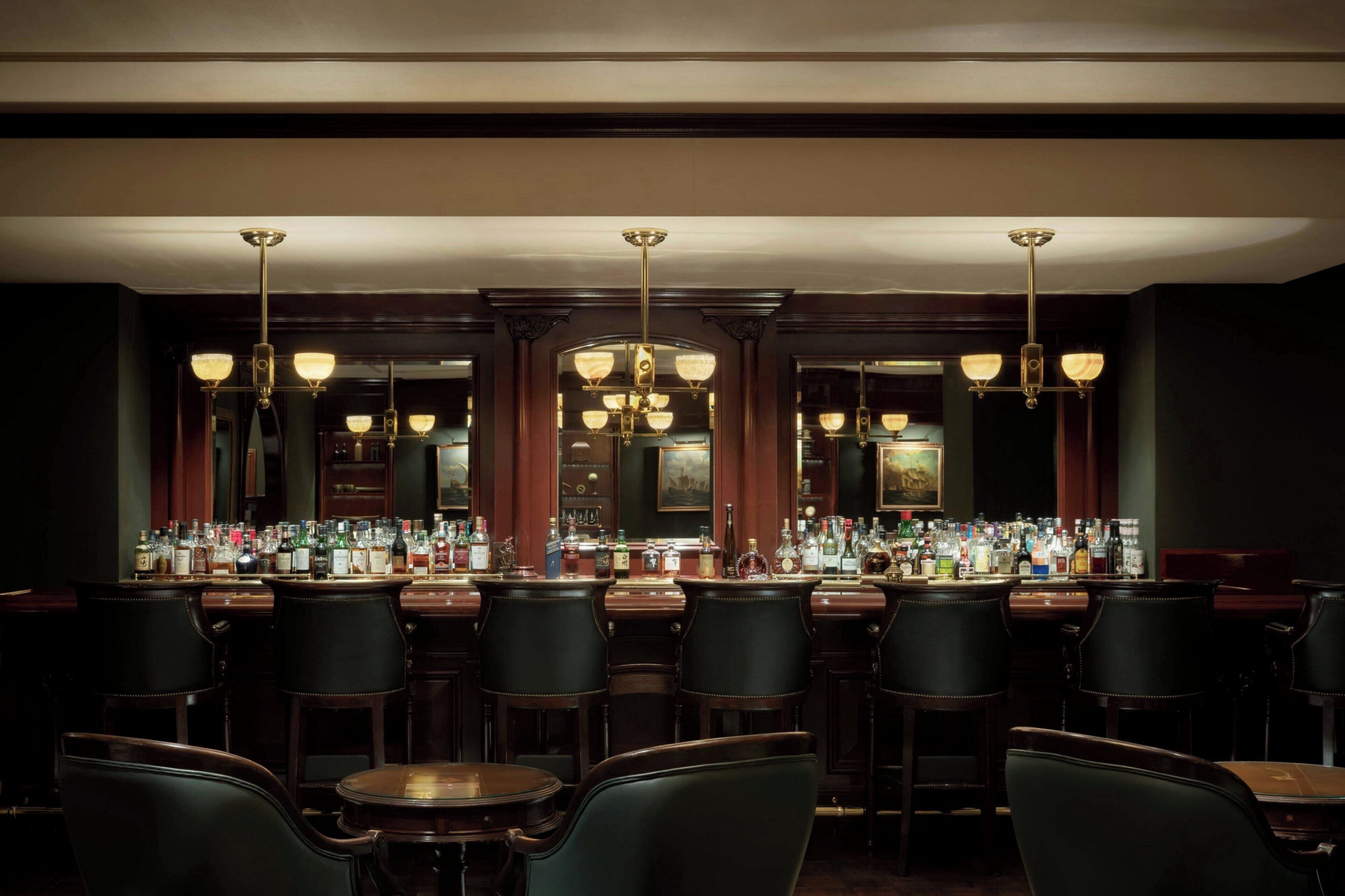 A bar area with multiple bar stools, a bar counter with various bottles, and a chandelier.
