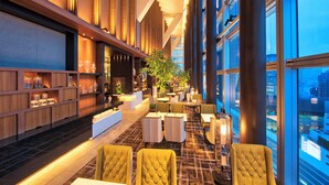 A modern hotel lobby with a high ceiling, large windows, and a mix of seating areas.