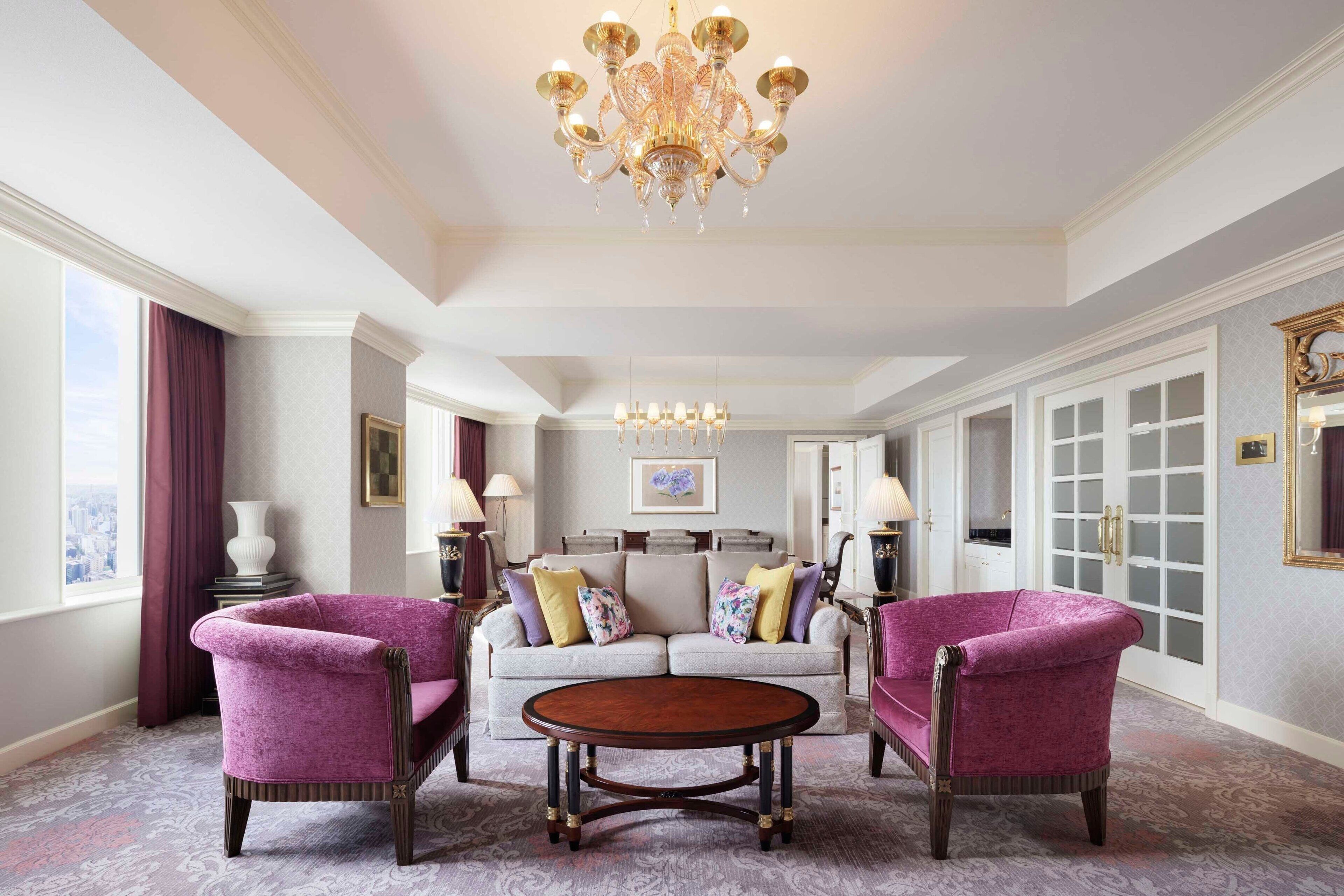 A spacious living room with a large chandelier, a sofa set, and two armchairs.