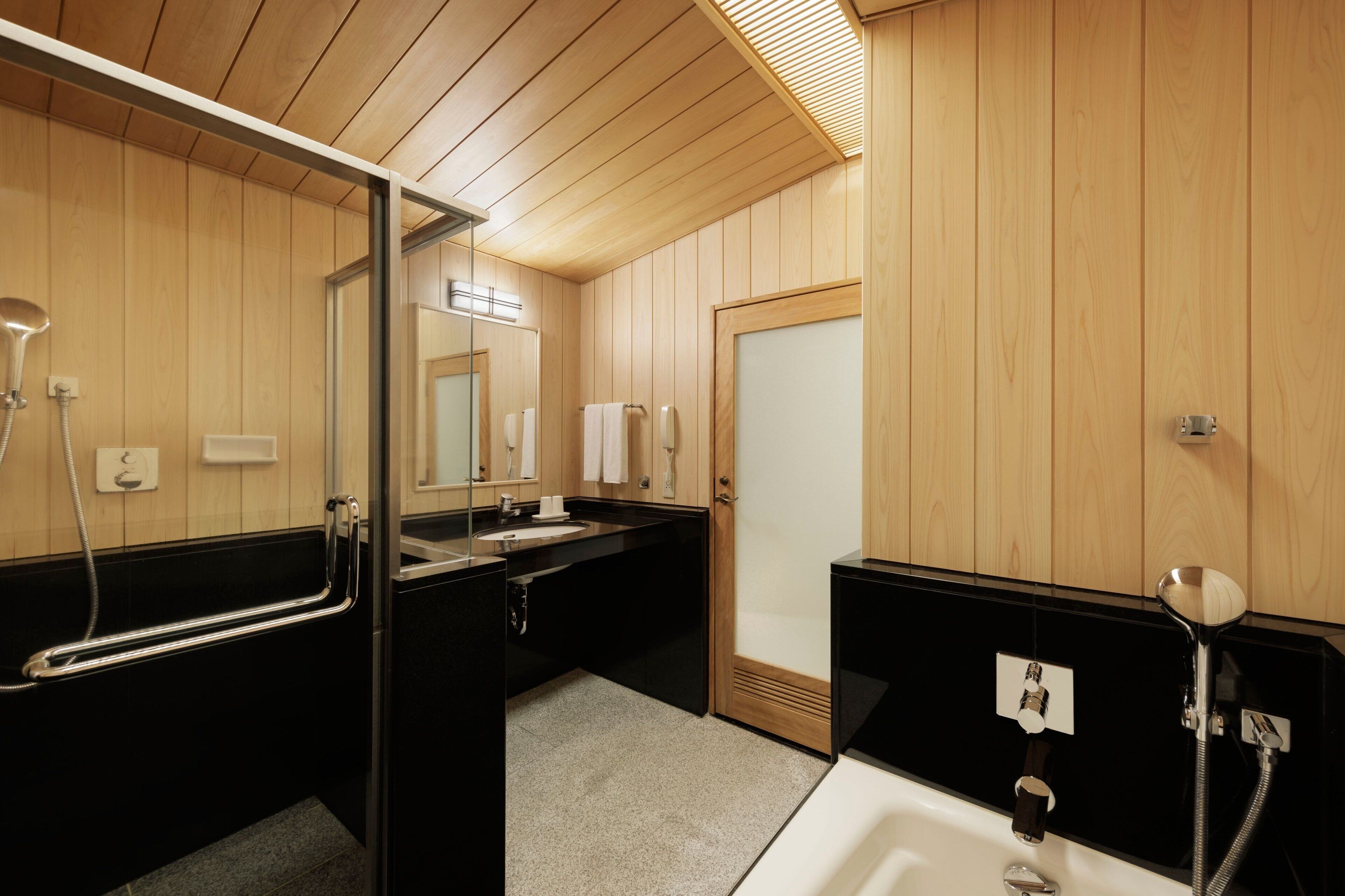 Un baño moderno con paneles de madera, cabina de ducha de vidrio, lavamanos negro y bañera blanca.