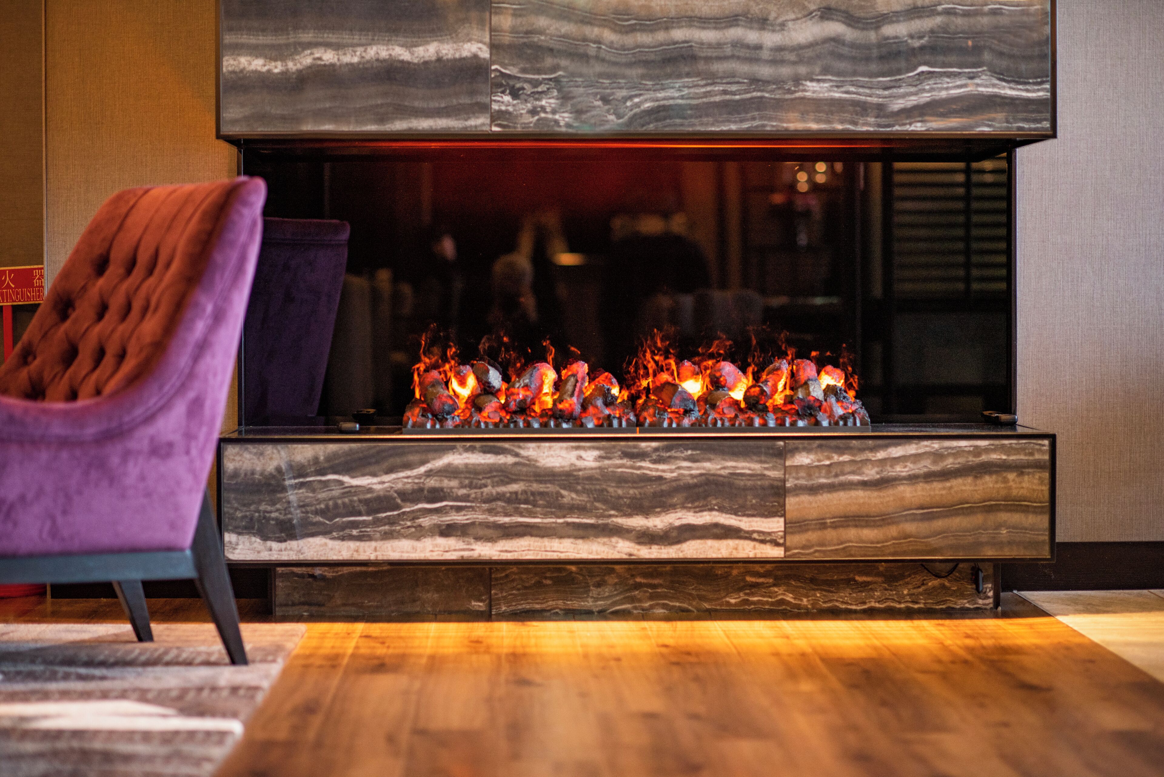 Una sala de estar moderna con chimenea empotrada, un sillón morado y piso de madera.