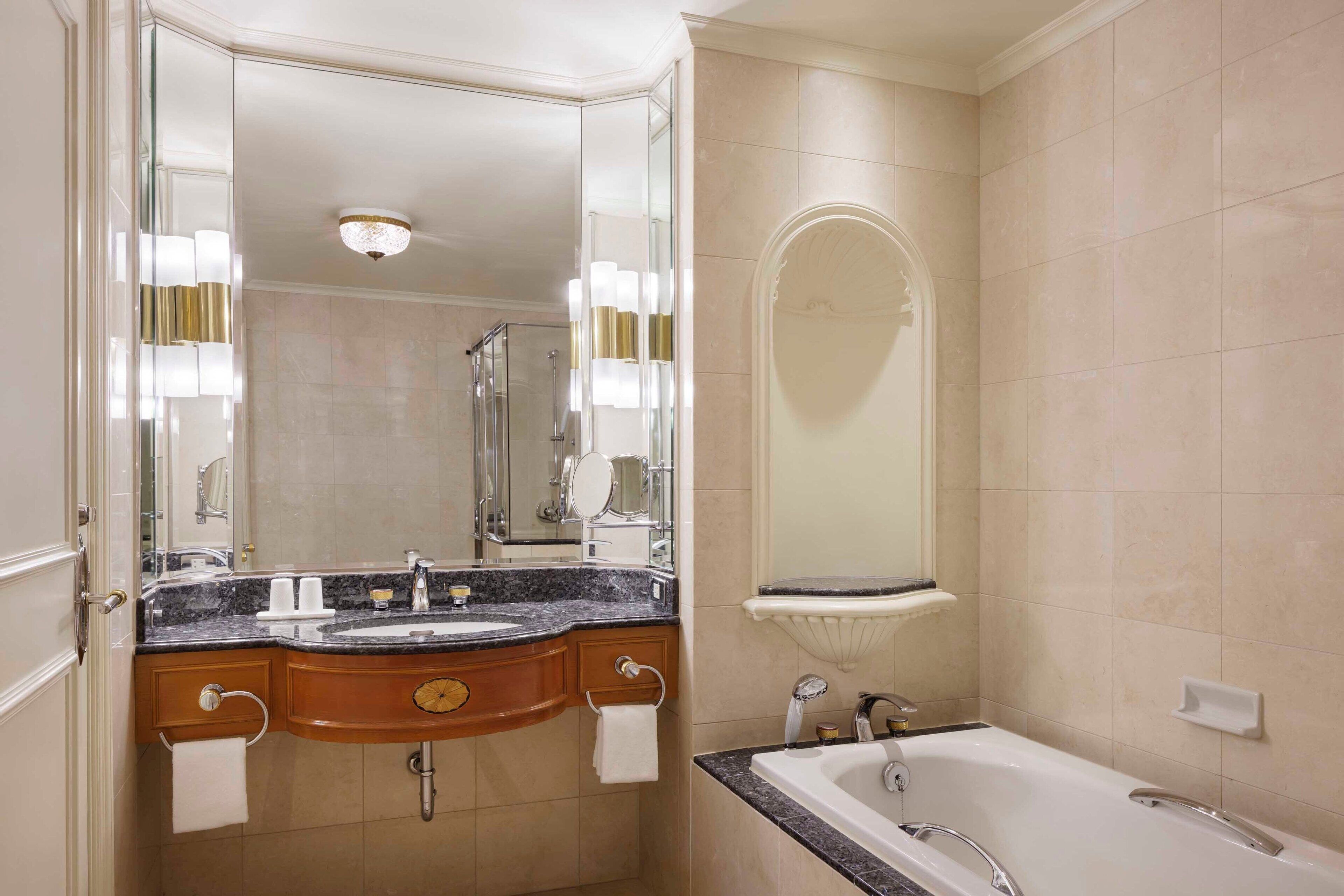 A bathroom with a marble sink, a large mirror, a bathtub, and a shower area.