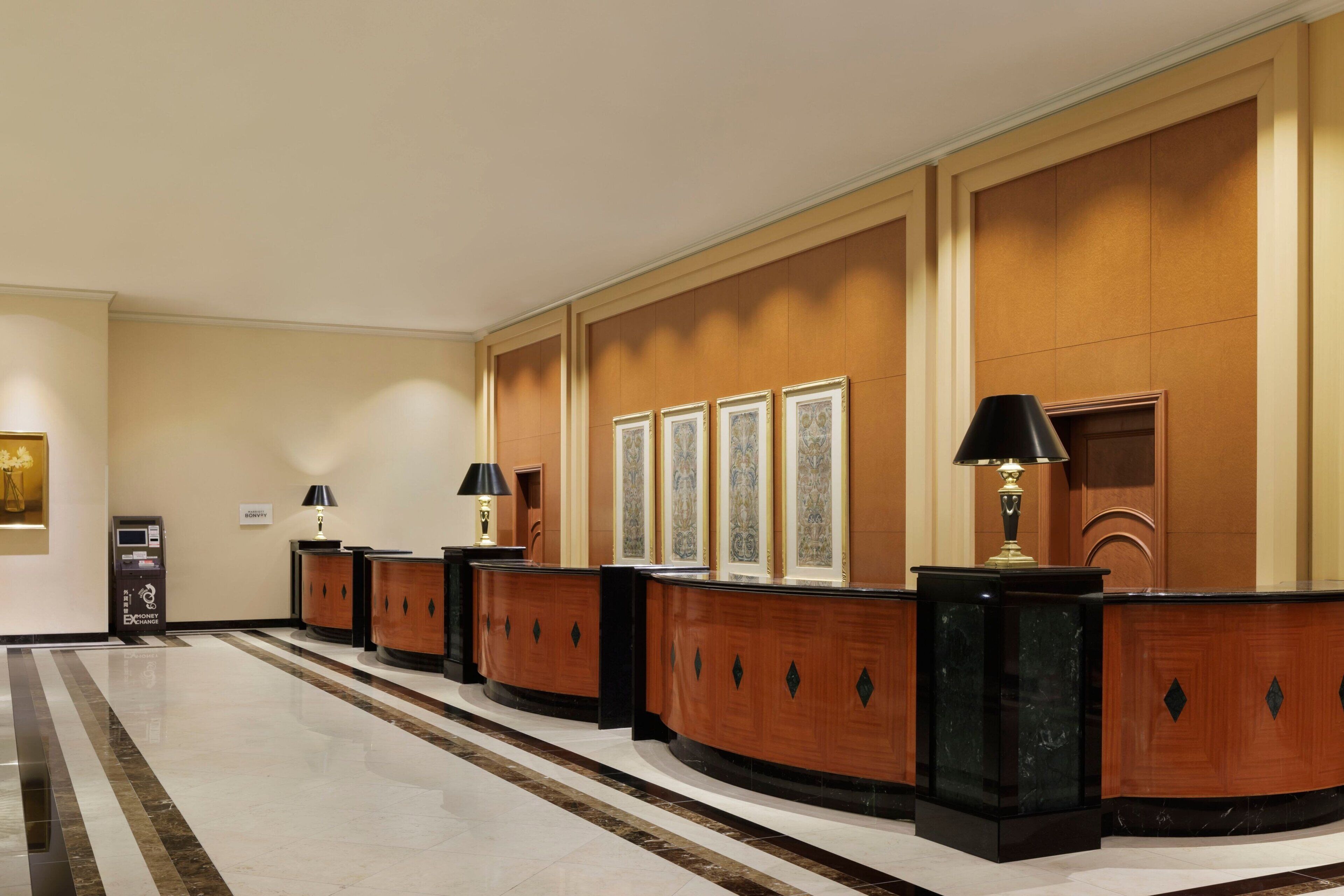 A reception area with a marble floor, wooden reception desks, framed artwork on the wall, and a cash machine.