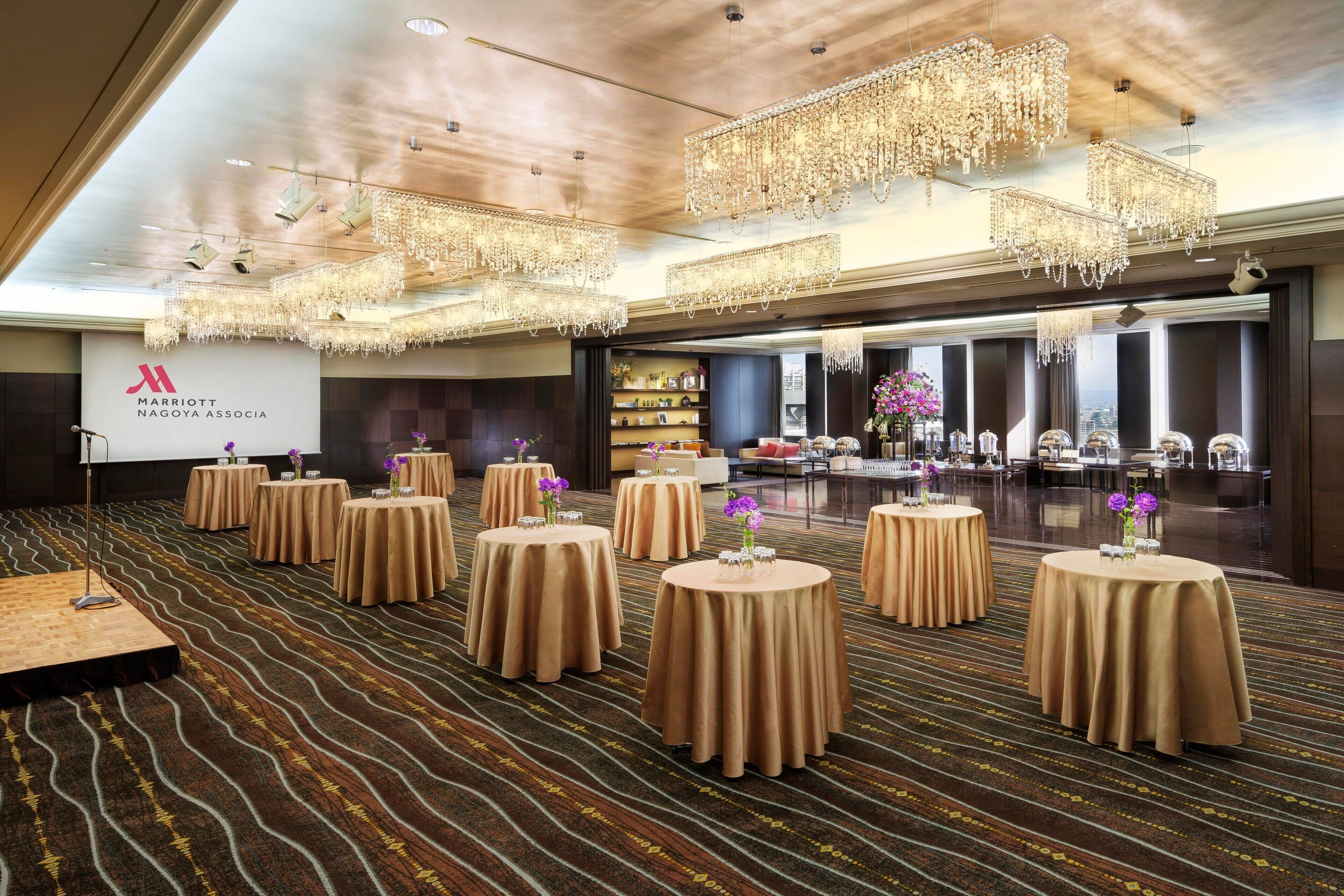 A spacious conference room with round tables, chandeliers, and a carpeted floor.